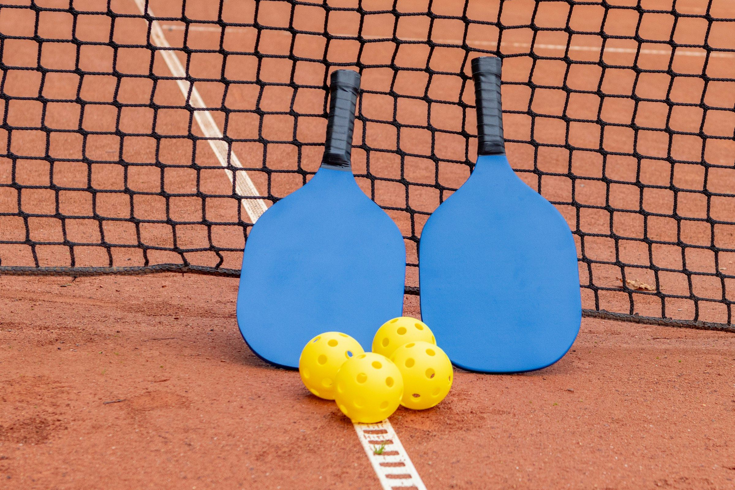 Two pickleball paddles and three balls on a court
